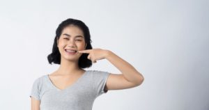 A lady is smiling brightly and pointing to her metal braces.