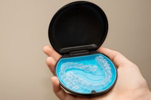 The clear dental aligners in their case are being held