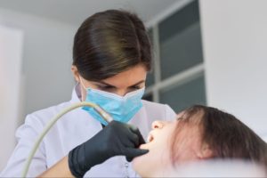 A masked dentist is performing a dental procedure on her patient