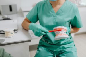 A dental professional is holding a dental model to demonstrate proper tooth brushing techniques.