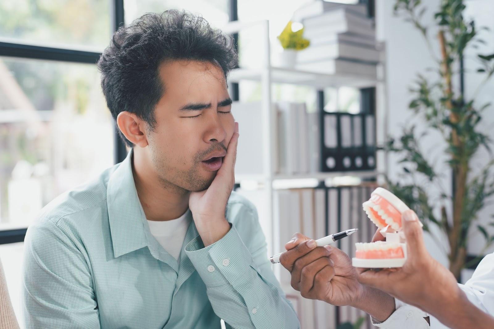 man having toothache as dentist shows a teeth model